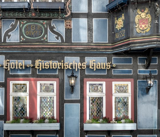 Fassade eines historischen Fachwerkhauses Blaue Ecke in Adenau mit verzierten Fenstern und Pflanzenkästen. Der Schriftzug "Hotel Historisches Haus" ist sichtbar., © Eifel Tourismus GmbH, Dominik Ketz Fassade eines historischen Fachwerkhauses Blaue Ecke in Adenau mit verzierten Fenstern und Pflanzenkästen. Der Schriftzug "Hotel Historisches Haus" ist sichtbar., © Eifel Tourismus GmbH, Dominik Ketz