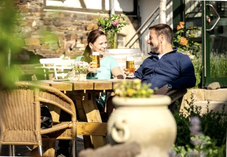 Wanderrast Gastronomie Eien Frau udn ein Mann mit einem Glas Bier sitzen in einem Biergarten und prosten sich zu