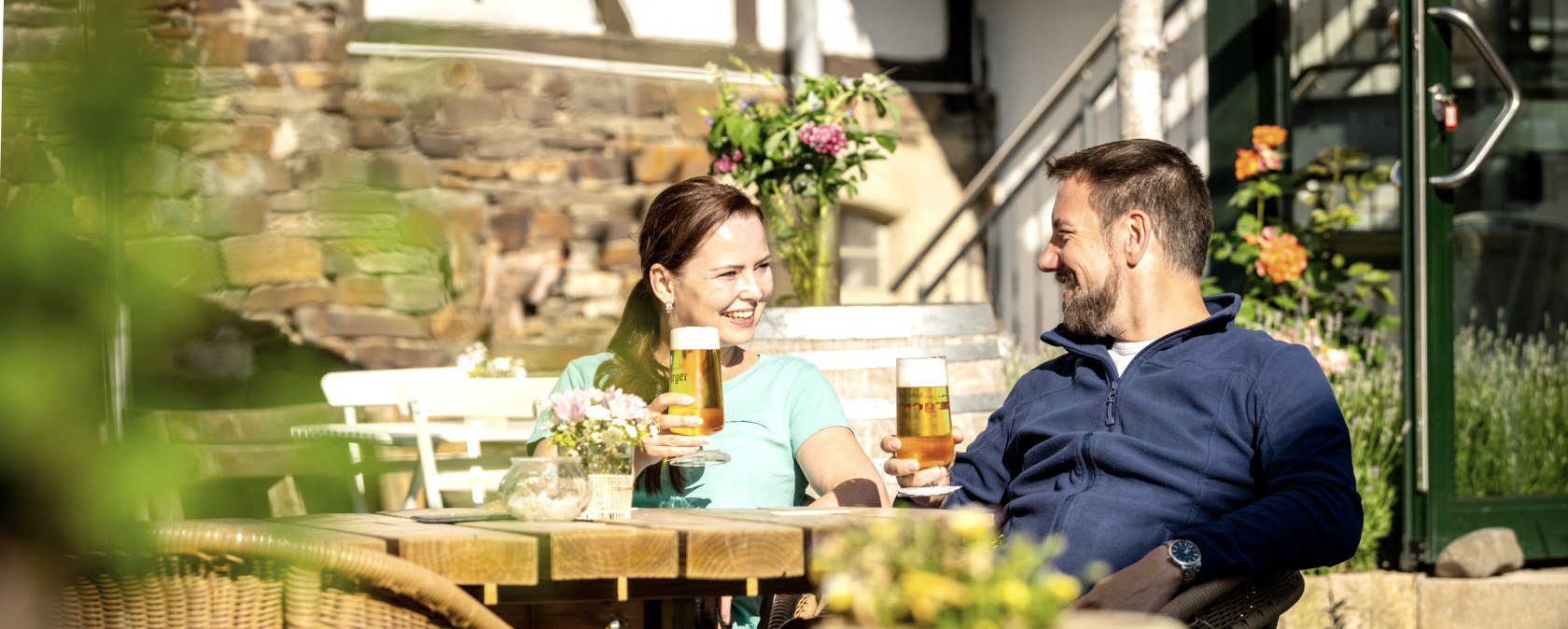 Wanderrast Gastronomie Eien Frau udn ein Mann mit einem Glas Bier sitzen in einem Biergarten und prosten sich zu