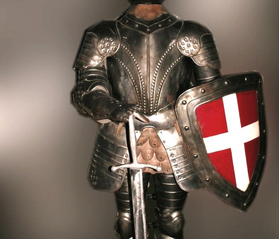 Een middeleeuws ridderharnas met zwaard en schild, met een wit kruis op een rode achtergrond, tegen een neutrale achtergrond., © Kerstin Coletta Een middeleeuws ridderharnas met zwaard en schild, met een wit kruis op een rode achtergrond, tegen een neutrale achtergrond., © Kerstin Coletta