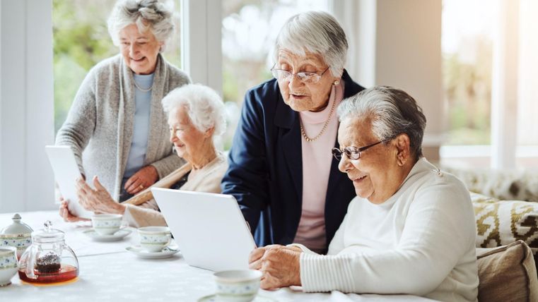 Eine Gruppe älterer Frauen sitzt an einem Tisch und nutzt Tablets. Sie scheinen interessante Aktivitäten zu teilen und haben eine fröhliche Ausstrahlung.
