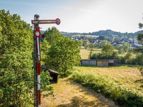 Een oud spoorwegsignaal staat in een weelderig landschap. Op de achtergrond zijn bomen en heuvelachtige weilanden zichtbaar.