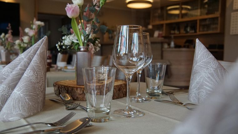 Ein elegant gedeckter Tisch mit Blumenarrangement und verschiedenen Gläsern. Die Tischdecke ist schlicht und harmonisch gestaltet.