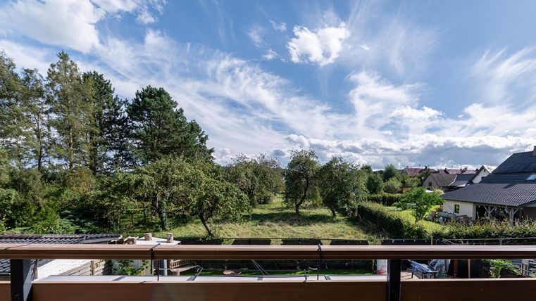 Een rustige landschap met bomen en een heldere lucht. Op de voorgrond is een balkon zichtbaar.
