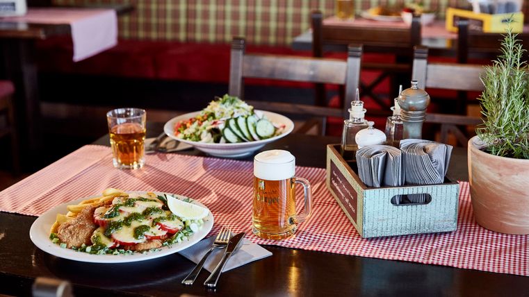Une table dans un restaurant avec deux assiettes de nourriture et deux verres de bière. L'arrière-plan est décoré de façon confortable et rustique.