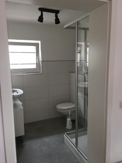 Une salle de bains moderne avec une douche, un lavabo et des toilettes. Les murs sont carrelés de manière claire et il y a une fenêtre pour la lumière du jour.