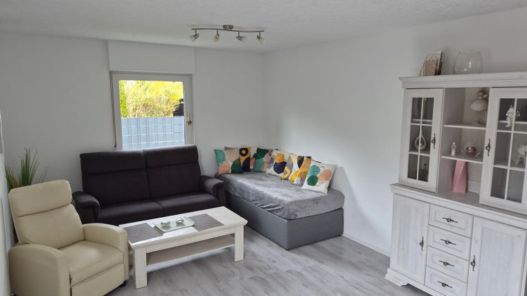 A bright living space with a comfortable couch and an armchair. A decorative cabinet stands against the wall, and the light filters through the window.