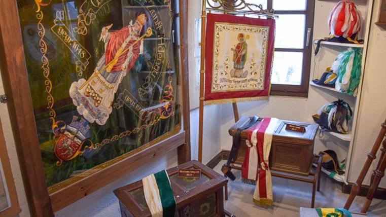 Eine Sammlung historischer Wappen und Fahnen in einem Ausstellungsraum. Im Hintergrund sind verschiedene Auszeichnungen und Dekorationen zu sehen.