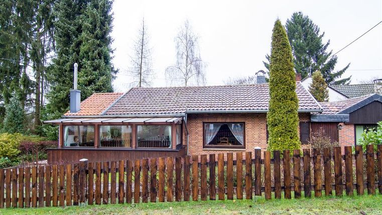 A cozy single-family home with a terrace and a well-maintained garden. Surrounded by trees and a wooden fence.