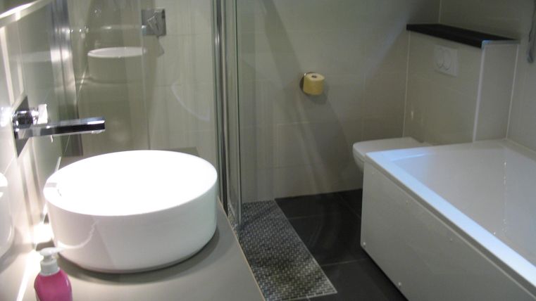 Ein modernes Badezimmer mit einer runden Waschschüssel und einer Duschkabine. Die Wände sind neutral gehalten und es gibt eine Badewanne neben der Dusche.