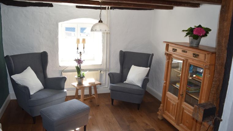 A cozy living space with two gray armchairs and a small table. Next to it, there is a wooden piece of furniture with a plant on top.
