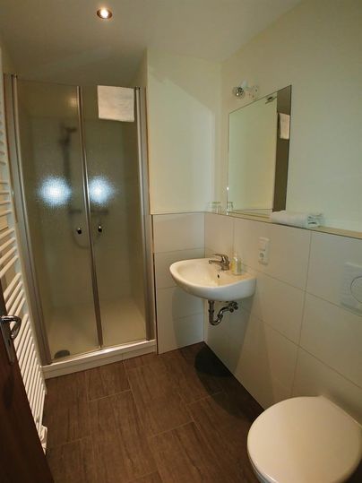 A bright bathroom with a shower, a sink, and a toilet. The walls are tiled, and the decor is modern.