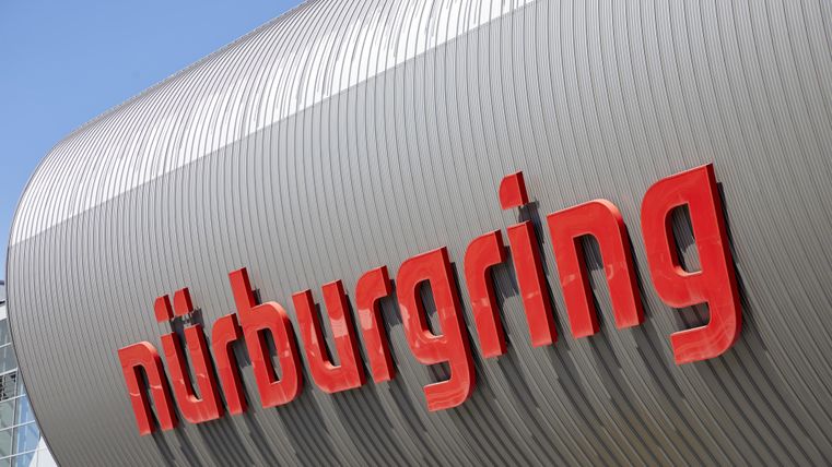 Das Bild zeigt das moderne Gebäude des Nürburgrings mit dem auffälligen roten Schriftzug. Der Himmel ist klar und der Fokus liegt auf der Architektur.