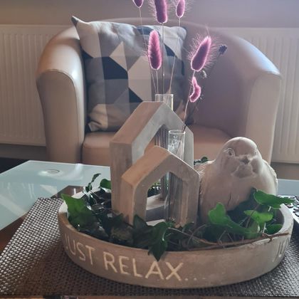 A decorative table with a round vessel that contains a carved bird and small plants. Above it is the inscription "JUST RELAX...".