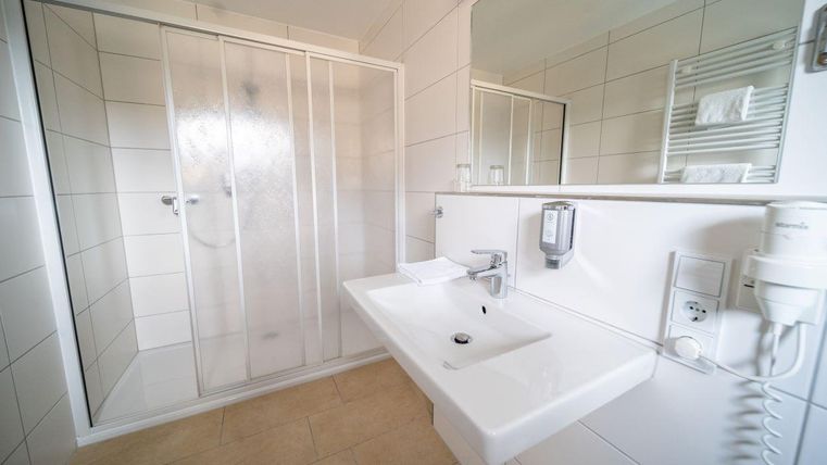 Een moderne badkamer met een douche en een wastafel. De muren zijn licht betegeld en het is goed verlicht.