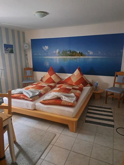 Une chambre avec un lit et des coussins colorés. Sur le mur, il y a une image d'une île tropicale.
