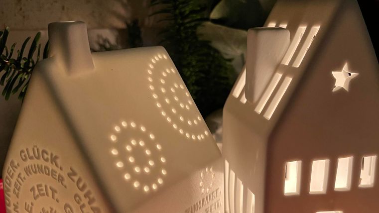 Deux maisons à bougies décoratives en céramique qui brillent doucement. L'une des maisons porte l'inscription "BONHEUR" et l'autre montre des fenêtres et une étoile.