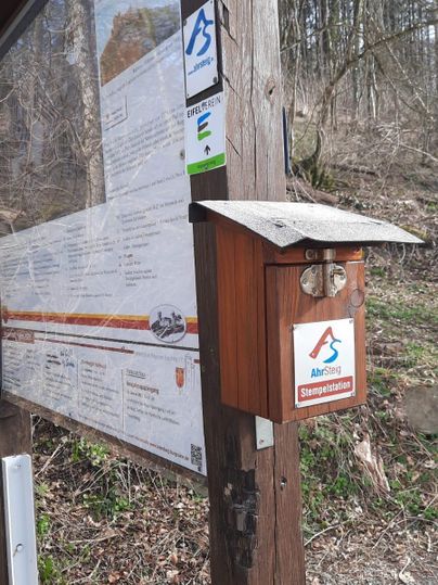 An information stand with a wooden box and a map board. The surroundings are natural and green.