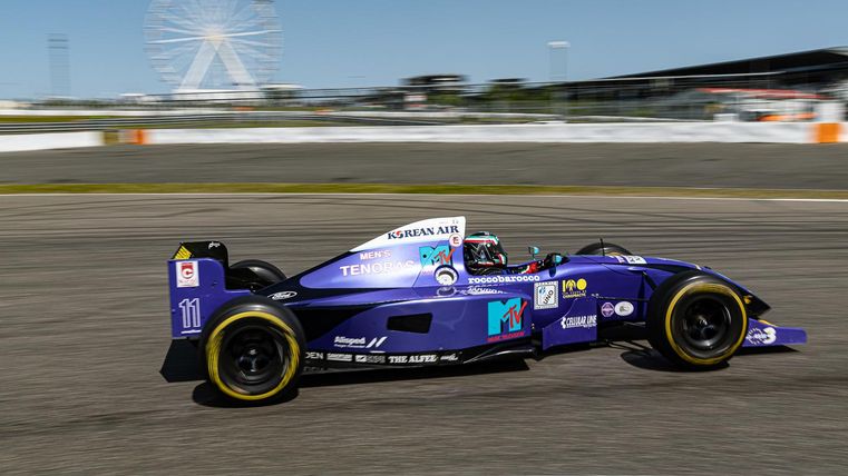 Ein schneller Rennwagen fährt auf einer Rennstrecke. Im Hintergrund ist ein Riesenrad zu sehen.
