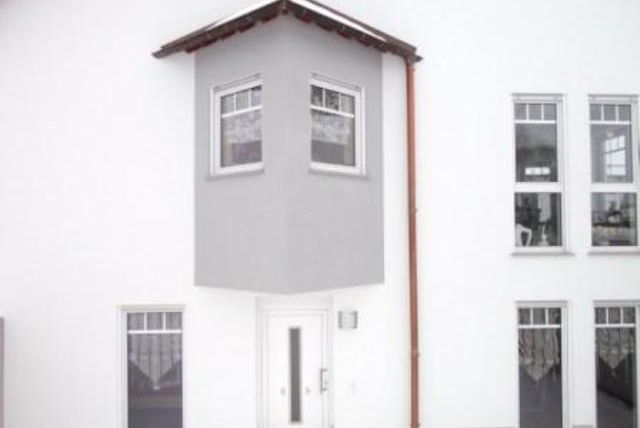 A modern building with a gray bay window and white walls. The windows are arranged symmetrically, which makes the appearance harmonious.