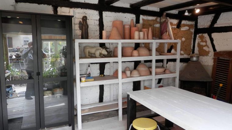 Een comfortabele kamer met een witte boekenwand die versierd is met potten en figuren. Een grote tafel en stoelen zijn zichtbaar op de voorgrond.