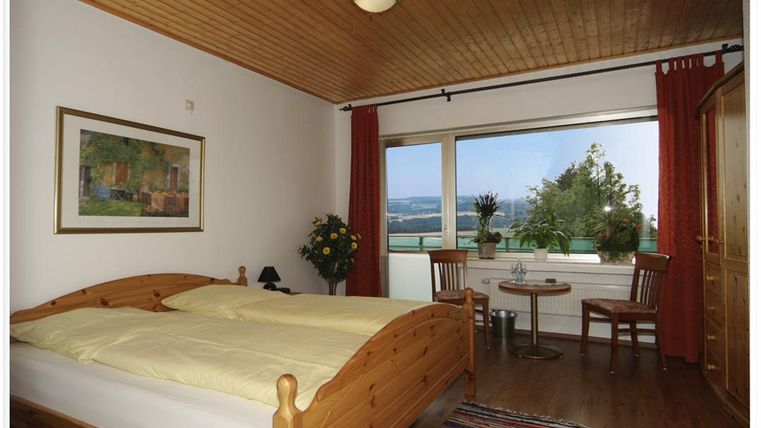A cozy bedroom with a large double bed and wooden decor. The window offers a beautiful view of the landscape.