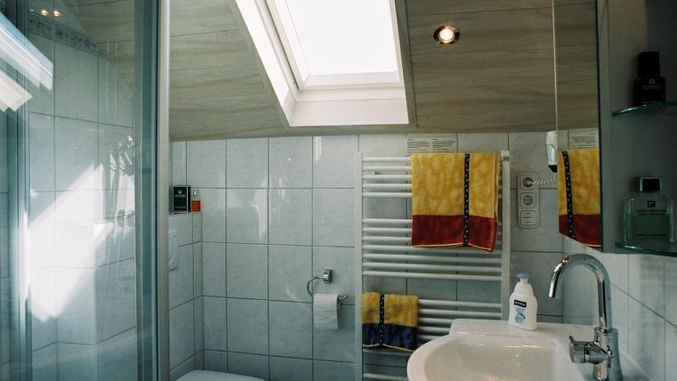 Een moderne badkamer met een douche en een raam voor daglicht. Handdoeken in geel en rood hangen aan een radiator.