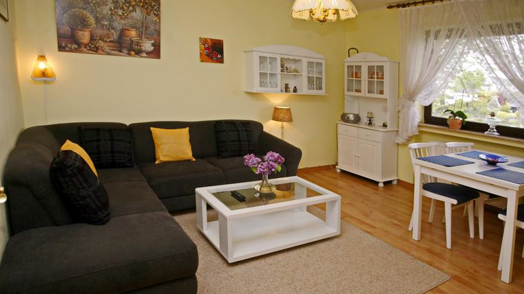 Een gezellige woonkamer met een grote, donkere bank en een witte salontafel. De ruimte is goed verlicht en heeft een uitnodigende eettafelgroep en decoratieve elementen aan de wanden.