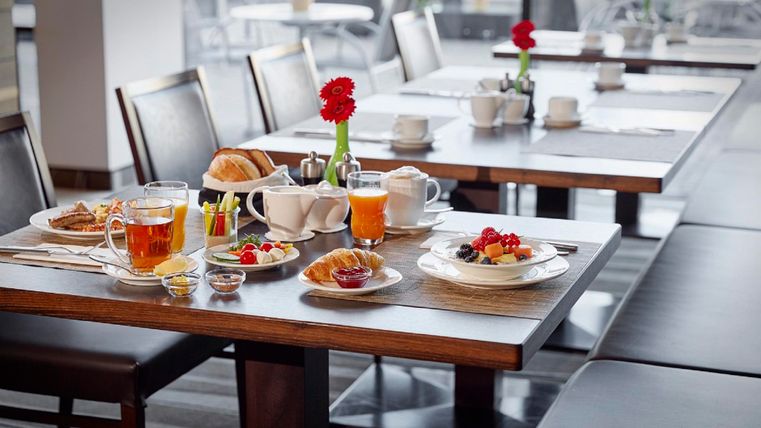 A beautifully set table in a restaurant with various dishes and drinks. On the table, fresh croissants, fruit, and teapots can be seen.