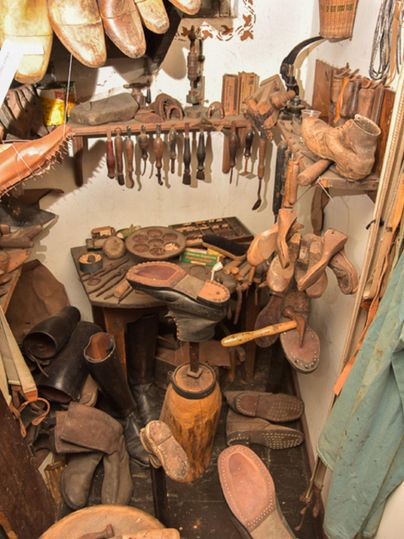 Eine Werkstatt mit verschiedenen Holzschuhen und Werkzeugen. Die Wände sind mit weiteren Materialien und Utensilien zum Schuhmachen dekoriert.