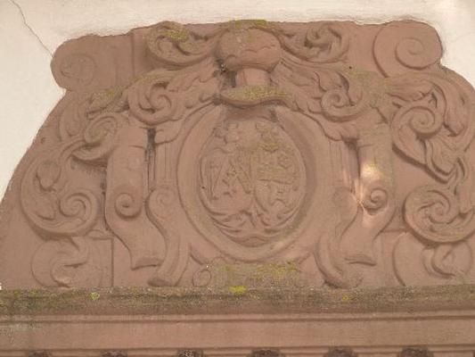 Ein kunstvolles Wappen mit verzierenden Elementen. Die Struktur ist aus Stein und zeigt feine Details.
