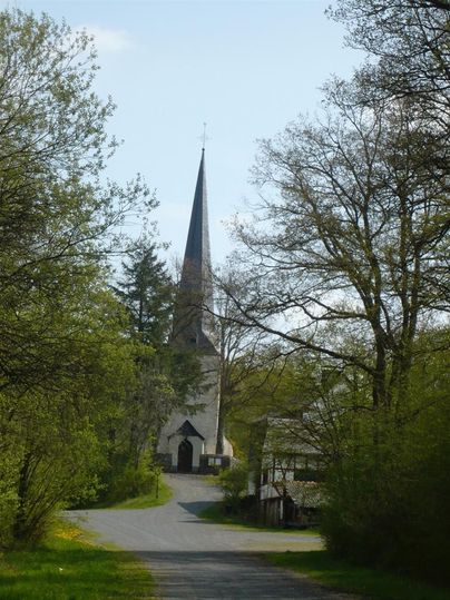A picturesque church with a pointed tower stands at the end of an avenue. Surrounded by trees and greenery, the scene radiates calm and peace.