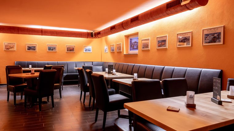 Een gezellig restaurant met oranje muren. Er zijn tafels en banken evenals schilderijen aan de muren.