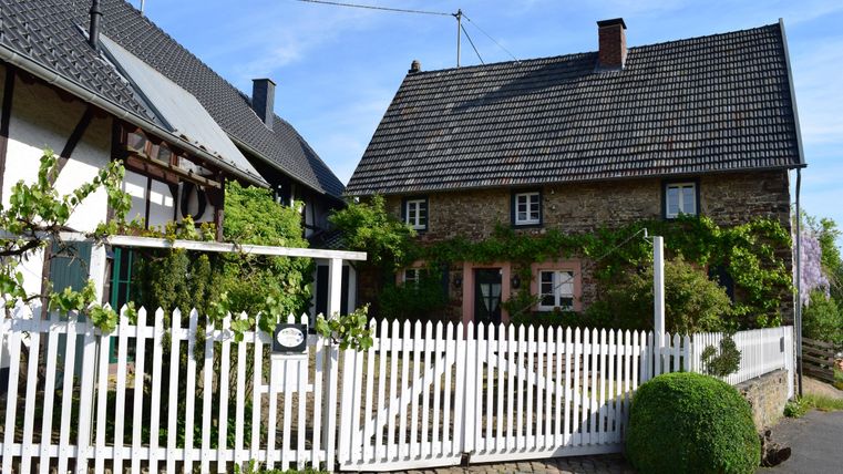 A charming house with green foliage and a white fence. The surroundings are bright and friendly, ideal for a rural atmosphere.