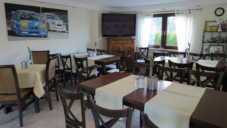 Un restaurant confortable avec des tables et des chaises en bois. Des images de voitures de course sont accrochées au mur, et de grandes fenêtres laissent entrer beaucoup de lumière naturelle.