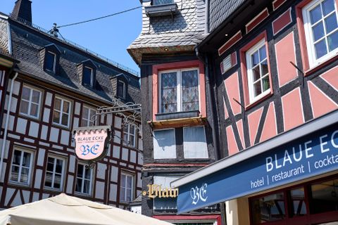 Ein malerisches Stadtbild mit Fachwerkhäusern und einem Restaurant namens "BLAUE ECKE". Die Gebäude sind in hellen Farben gehalten und laden zum Verweilen ein.