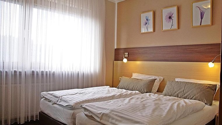 Une chambre lumineuse avec deux lits simples et une décoration moderne.
De douces rideaux et des images décoratives créent une atmosphère agréable.