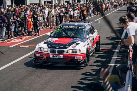 Ein Rennwagen fährt auf der Strecke vorbei an einer großen Menge von Zuschauern. Die Atmosphäre ist aufregend und lebhaft.