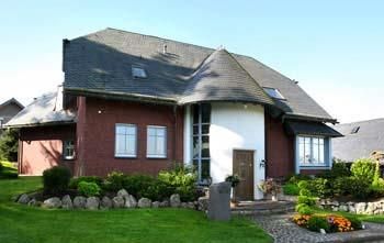 Une maison moderne avec un mélange de façades rouges et blanches. Le jardin est bien entretenu et décoré de plantes et de fleurs.