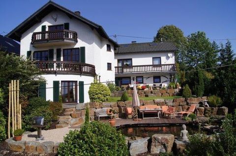 Een mooi huis met meerdere balkons en een tuin. In de tuin is er een vijver en een zonnig terras met meubels.