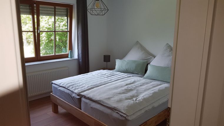 Ein gemütliches Schlafzimmer mit einem Doppelbett und frischen Bettdecken. Viel Tageslicht fällt durch das Fenster, das einen Blick nach draußen bietet.