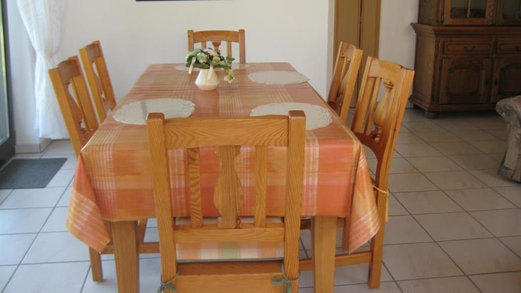 Une salle à manger confortable avec une grande table en bois et huit chaises. La nappe est orange et la pièce dispose de beaucoup de lumière naturelle.