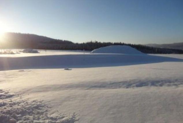 A snowy landscape under a clear blue sky. The sun is shining and there are gentle hills of snow.