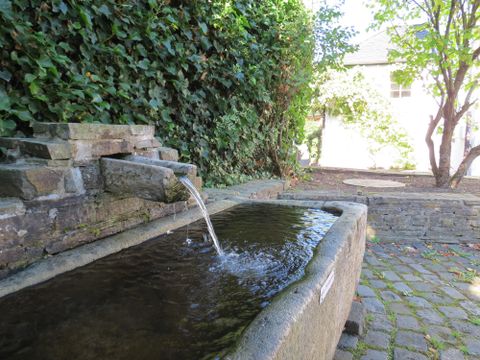 Ein schöner Steinbrunnen in einer grünen Umgebung. Das Wasser sprudelt sanft in das rechteckige Becken.