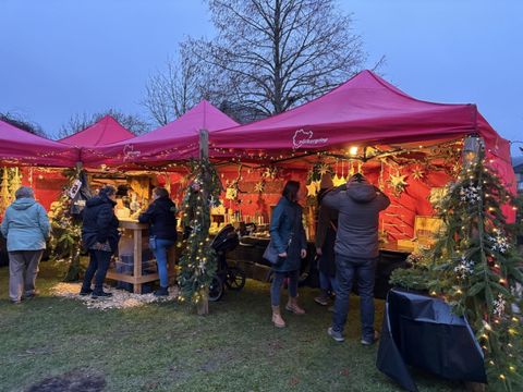 Ein festlicher Weihnachtsmarkt bei Nacht mit vielen Menschen. Im Mittelpunkt steht ein beleuchteter Weihnachtsbaum und rote Markisen.