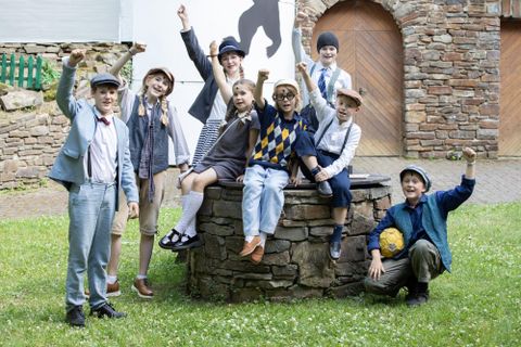 Eine Gruppe von Kindern steht fröhlich um einen Brunnen. Alle haben Spaß und posieren mit erhobenen Armen.