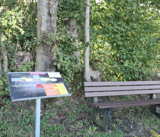 A wooden bench stands next to an information sign in front of a green hedge and trees., &copy; TI Hocheifel-N&uuml;rburgring