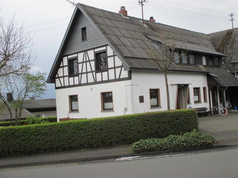 Ein traditionelles Fachwerkhaus mit einem grauen Dach. Es steht in einer ruhigen Umgebung mit einer grünen Hecke.