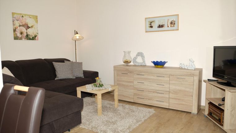 Un salon lumineux avec un canapé confortable et un armoire en bois. Sur la table se trouve un vase et la télévision est placée dans le coin.