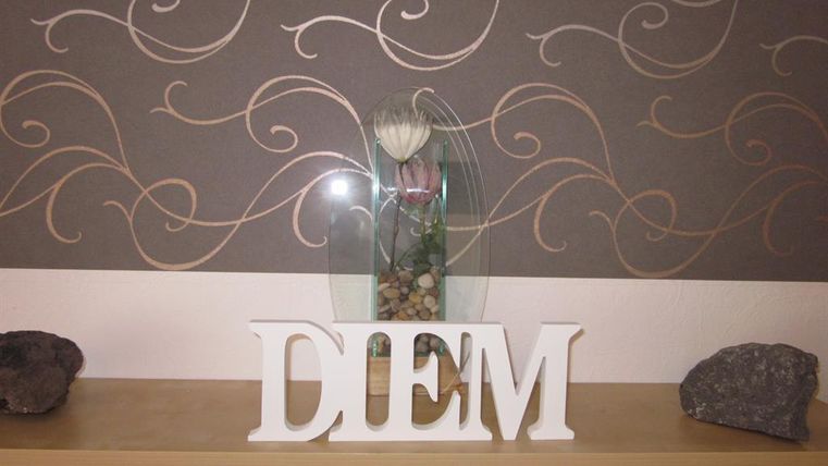 Een elegante decoratie met het woord "DIEM" in witte letters. Op de achtergrond is er een stijlvolle muur met een gebogen patroon en een bloemenvaas.